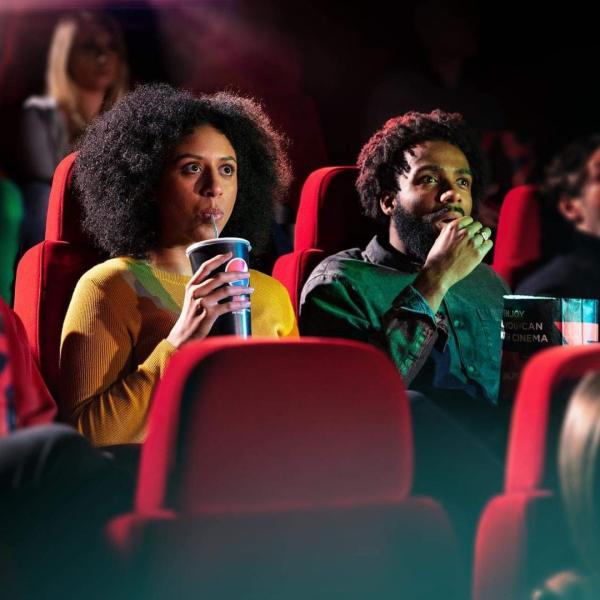 Couple eating popcorn and drinking Pepsi Max in the audience of a cinema screen.