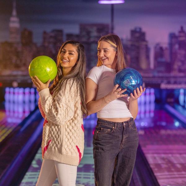Two girls are pictured holding different colour bowling balls in a bowling alley